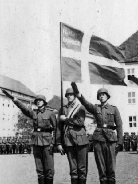 Medlemmer af Frikorps Danmark står under en modificeret udgave af Dannebrog og heiler i 1941.